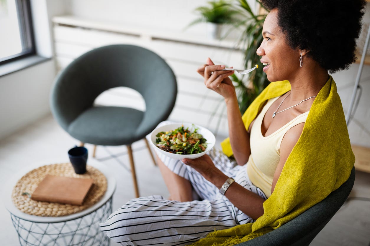Woman sits back on a couch while eating a bowl with a healthy plant-based salad