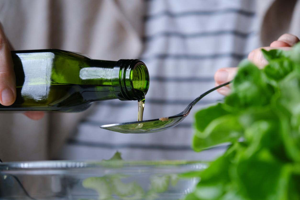 Someone pouring olive oil into a spoon over a bowl of salad