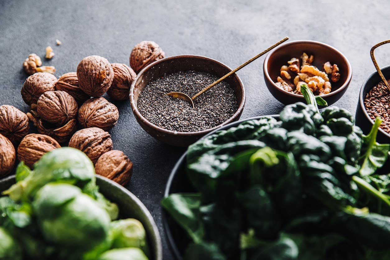 Close-up of omega 3 vegan food in bowls on black table: walnuts, chia seeds, nuts, and leafy greens