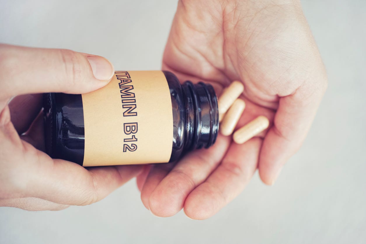 Hands pouring out a few vitamin b12 supplements from a plastic container